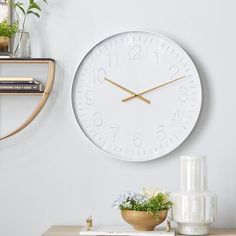 a white clock sitting on top of a wooden table next to a vase filled with flowers