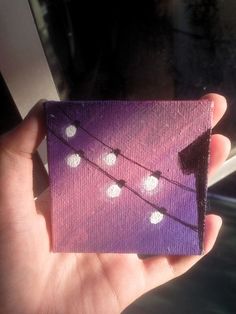 a hand holding up a small purple square with white polka dots on it and a string of lights