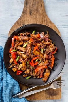 a skillet filled with meat and vegetables on top of a wooden cutting board next to a blue towel