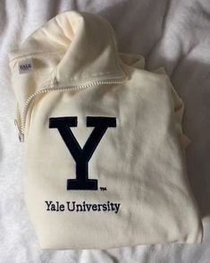 a white hoodie with the y on it is laying on a bed next to a pair of scissors