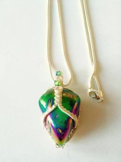 a necklace with a green and purple glass object on it's back end, sitting on a white surface