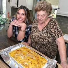 two women standing in front of a pan of food on top of a kitchen counter