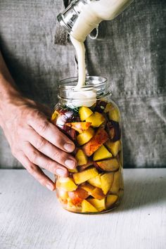 a person pouring milk into a jar filled with fruit