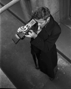 a man holding an old camera up to his face while looking down at the ground