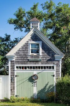 a small gray and white building with a clock on it's face next to trees