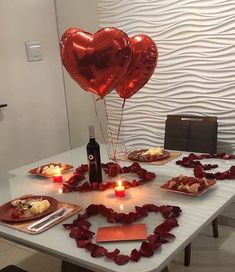 two heart shaped balloons sitting on top of a table next to plates with food and candles