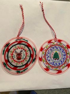 two paper plates with christmas designs hanging from strings on a piece of paper that is taped to the wall