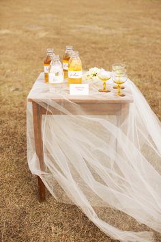 the table is covered with white tulle and bottles of honey on it, along with flowers