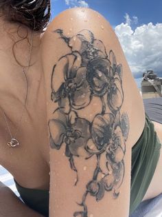 a woman laying on the beach with her arm covered in flowers and leaves tattoo design