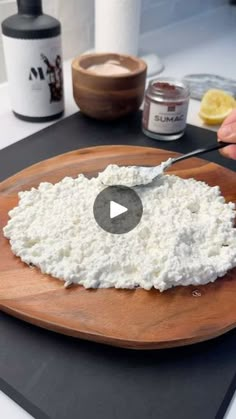 a person is spreading cheese on top of a cutting board with a knife and some other ingredients in the background