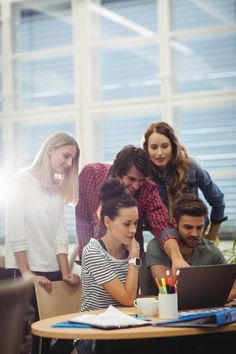 a group of people gathered around a table looking at a laptop computer with pens and pencils on it