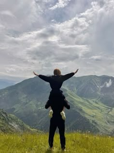 a man holding a child in his arms while standing on top of a grass covered hill