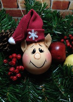 a christmas ornament with a smiling face on it's head, surrounded by pine cones and other holiday decorations