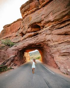 a woman is walking down the road in front of a rock formation that looks like an arch