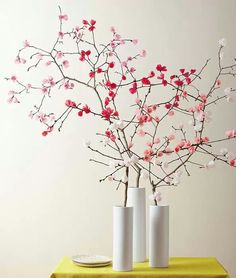 two white vases with pink flowers in them on a table next to a wall