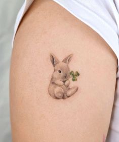 a small tattoo of a rabbit holding a leaf on the side of a woman's thigh