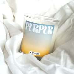 a candle sitting on top of a white bed covered in blankets and sheets with the word purpr