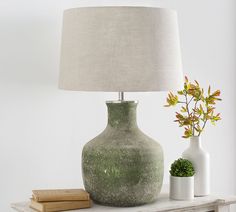 a green vase sitting on top of a wooden table next to a lamp and books