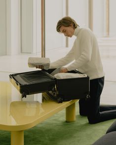 a woman is packing her suitcase on a table in the living room with green carpet