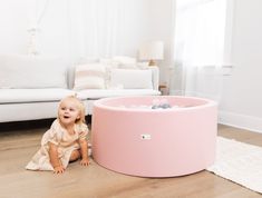 a baby sitting on the floor next to a pink tub