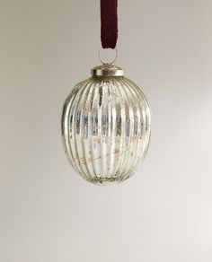 a glass ball ornament hanging from a red cord on a white wall background