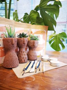 three clay pots with plants in them on a table next to some markers and pens