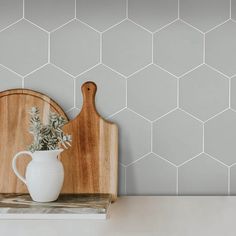 a wooden cutting board sitting on top of a counter next to a white vase filled with flowers