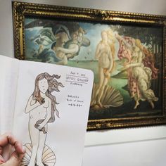 a person holding up a drawing in front of a wall with paintings and artwork on it