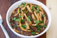 a white bowl filled with french fries covered in gravy and garnished with parsley