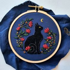 a black cat sitting on top of a blue cloth next to a hoop with flowers