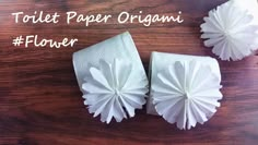 two white paper origami flowers sitting on top of a wooden table