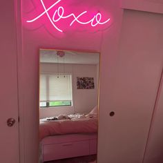 a pink room with a neon sign above the bed and a mirror on the wall