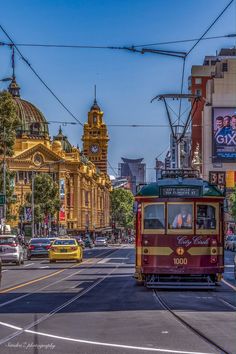 a red trolley car traveling down a street next to tall buildings and cars driving on the road