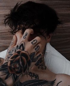 a man with tattoos covering his face and holding his hand up to his ear while laying in bed