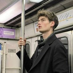 a young man standing on a subway train holding onto the handle bars and looking up