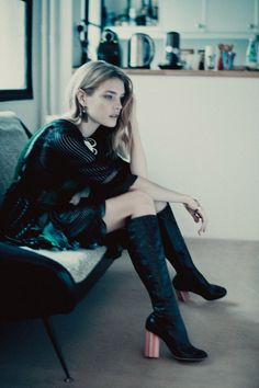 a woman sitting on top of a chair wearing high heeled boots and black dress