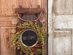 a welcome sign hangs on the front door of an old building with wreaths hanging from it