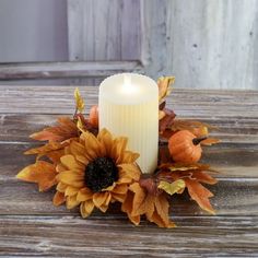 a white candle sitting on top of a wooden table next to leaves and pumpkins