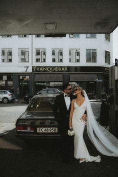 a bride and groom standing in front of a car