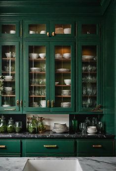 a kitchen with green cabinetry and marble counter tops, gold trim on the glass doors