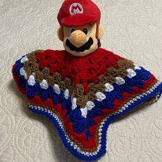 a crocheted blanket with a stuffed animal wearing a baseball cap on top of it