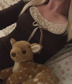 a woman laying in bed with a stuffed deer on her stomach and wearing a brown shirt