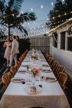 a long table set with plates and place settings for an outdoor dinner party in the evening