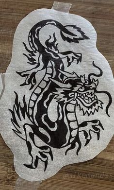 a black and white drawing of a dragon on a piece of wood with some paint