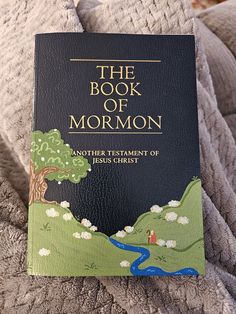 the book of mormon is sitting on top of a blanket with a river running through it