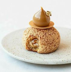 a small dessert on a white plate with a brown sauce in the middle and a gold decoration on top