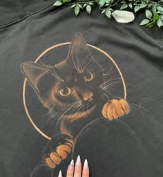 a woman's hand on top of a black t - shirt with a drawing of a cat