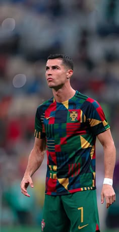 a soccer player is looking up at the ball in his hand while wearing a colorful shirt and shorts