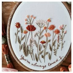 a close up of a embroidery on a wooden hoop with flowers and yarn in the background