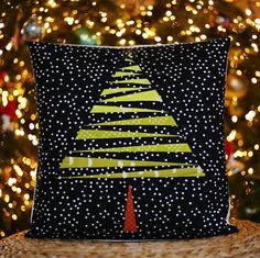 a christmas tree pillow sitting on top of a table next to a christmas tree with lights in the background